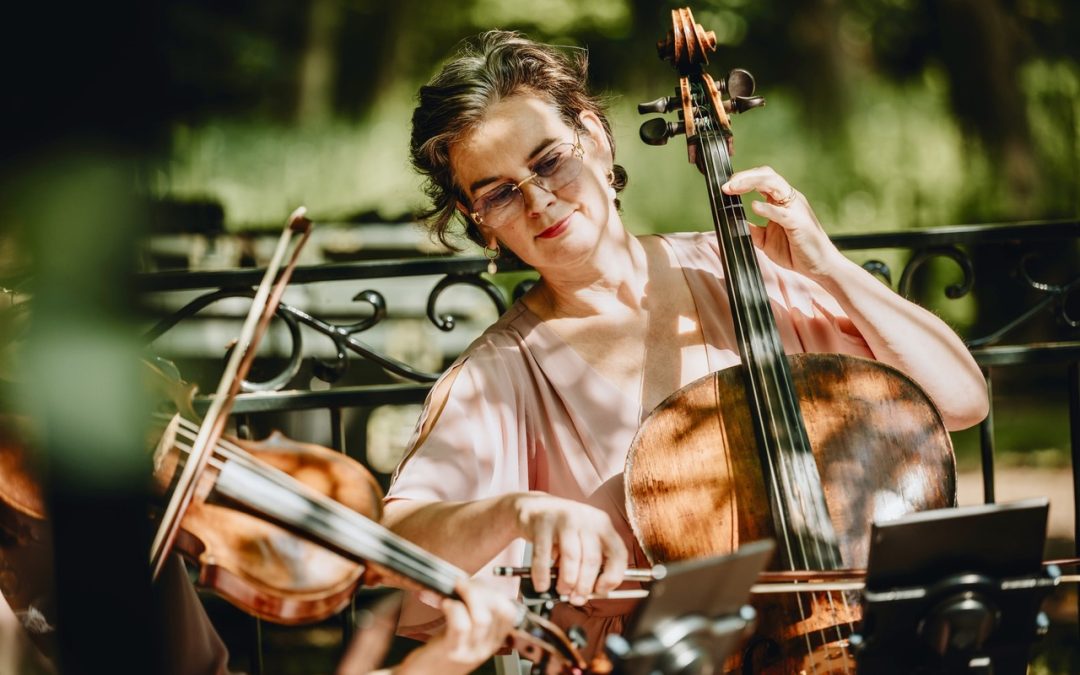 Celliste speelt cello tijdens een sfeervol buitenoptreden in het groen, onderdeel van een strijkkwartet tijdens een bruiloft of evenement.