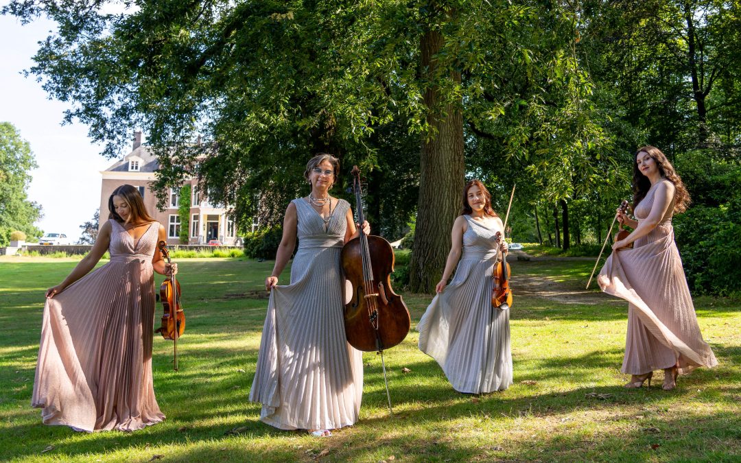 Scarlett staat met haar cello op een grasveld, samen met drie andere mensen.