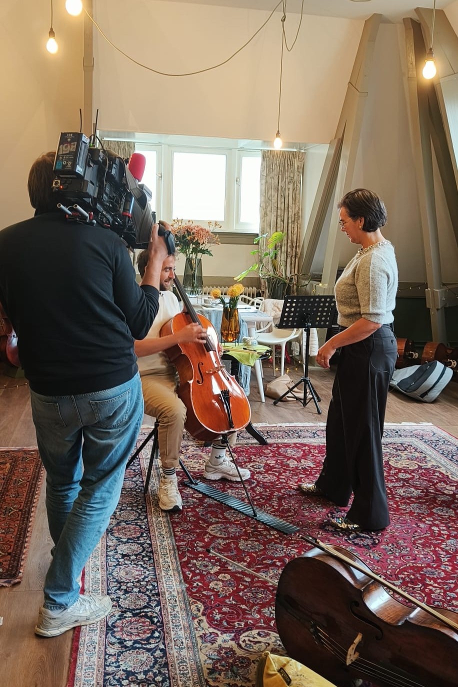 Presentator Daniël van Editie NL speelt zijn eerste noten op de cello, met Scarlett naast hem en een RTL 4-cameraman die filmt